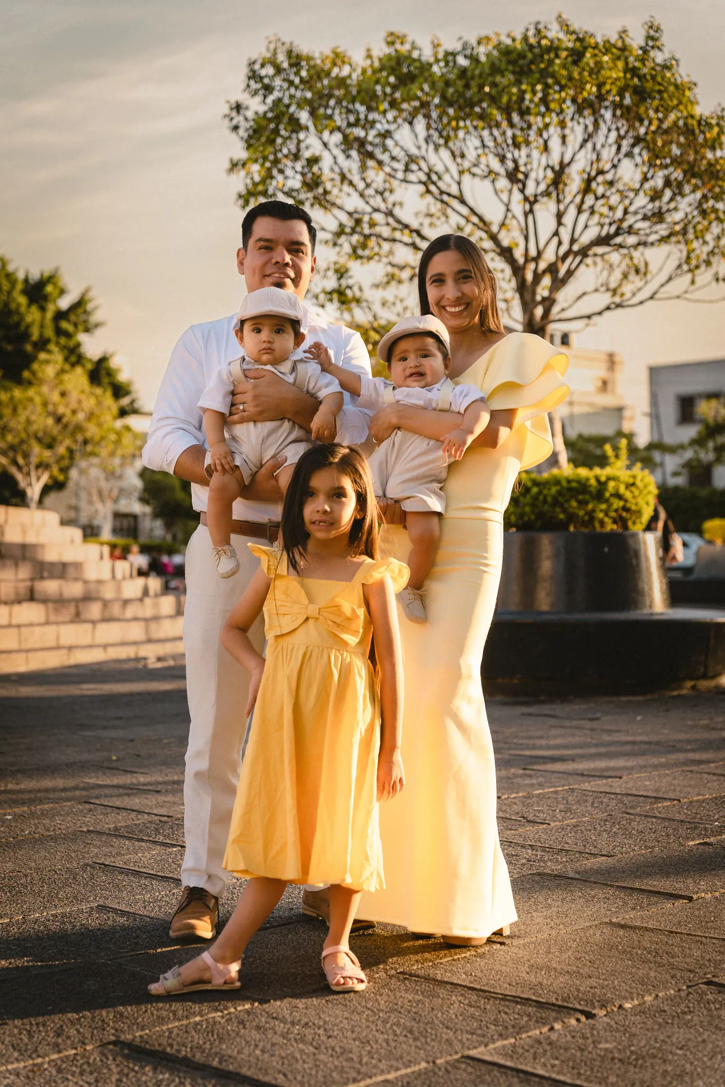 A mother and father in the evening sun, each holding a baby, with their daughter in a yellow dress in front