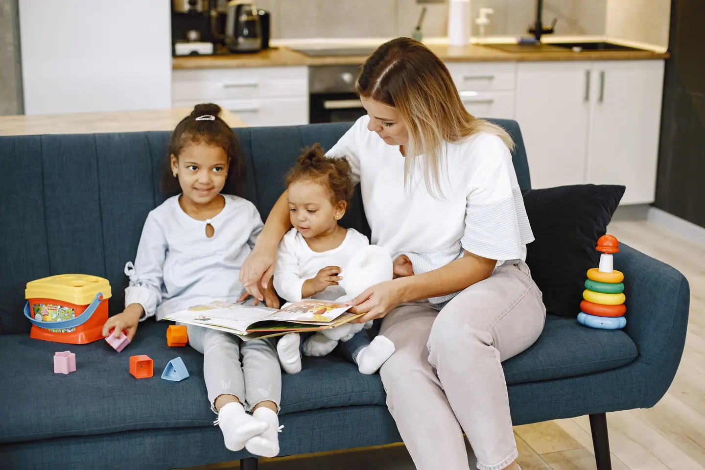 A nanny reading a picture book on a sofa with two young children